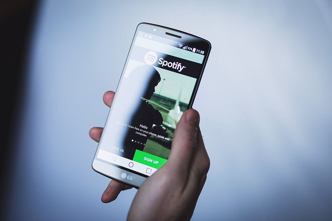 A hand holds an LG smartphone displaying the Spotify welcome screen in 2016