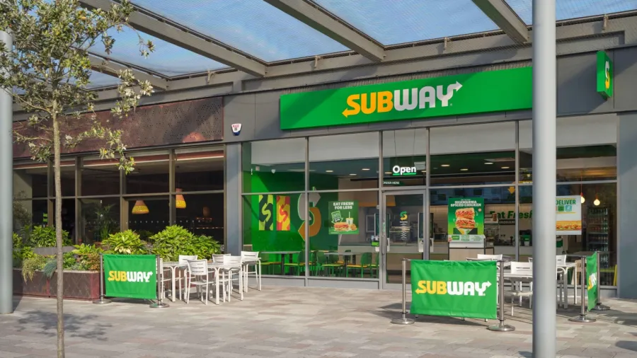 Subway restaurant exterior with green-and-yellow signage and outdoor seating.
